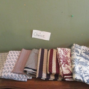 May include: A selection of folded fabric pieces with various patterns, including floral, geometric, and striped designs. Colors range from blue and white to burgundy and cream. A handwritten note reads "Choice".