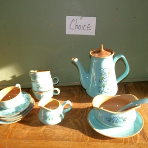 May include: A vintage tea set in shades of turquoise and brown, featuring a teapot, creamer, sugar bowl, cups, and saucers. The set is decorated with a floral pattern. The word "Choice" is written on a small white card.