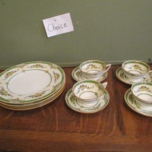May include: A vintage tea set with a floral design. The set includes four teacups with saucers and four plates. The rims are decorated with a green border and floral accents. The word "Choice" is written on a white paper.