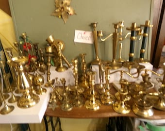 Peut inclure: Une collection de bougeoirs en laiton de différentes tailles et formes. Certains ont plusieurs bras, d'autres sont à tige unique. Les bougeoirs sont disposés sur une surface en bois, avec un panneau indiquant "Choice".