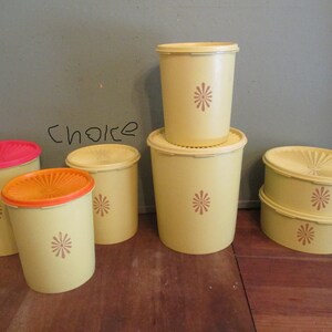 May include: A collection of vintage yellow plastic food storage containers with lids in various sizes. Some lids are red or orange. Each container has a brown floral design. The word "choice" is written on the wall behind the containers.