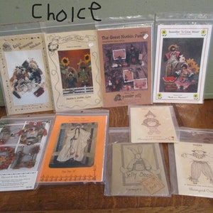 May include: A collection of craft pattern packets in clear plastic sleeves. The packets feature various designs, including scarecrows, sunflowers, and other folk art themes. The word "Choice" is written at the top.