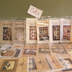 May include: A collection of craft patterns, including cross-stitch and quilting designs. The patterns feature various themes, including Americana, nature, and seasonal motifs. The word "Choice" is written on a small white sign.