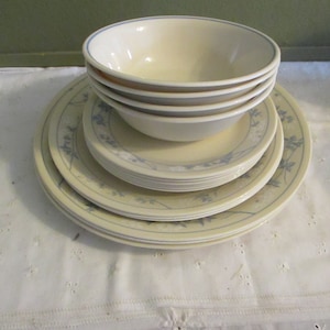 May include: A stack of white ceramic plates with a blue floral design. The plates are stacked on top of each other, with a bowl on top of the stack.
