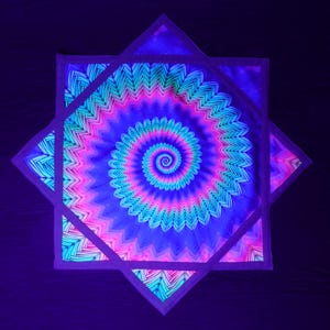 Puede incluir: Un diseño geométrico vibrante con un centro en espiral, que irradia en tonos de azul, rosa y verde. La obra de arte está enmarcada dentro de una estructura en forma de estrella, creando un efecto psicodélico hipnotizante. La pieza brilla bajo luz negra.