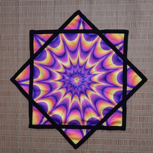 Puede incluir: Una tela en forma de estrella de color morado y amarillo con un borde negro. La tela tiene un patrón de remolino que crea una ilusión óptica.