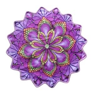 Peut inclure: Un tapis en tissu circulaire à bord festonné présentant un motif mandala vibrant dans des tons de violet, magenta et vert citron. Le design se compose de pétales floraux concentriques et de motifs circulaires pointillés rayonnant du centre.