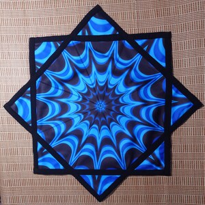 Puede incluir: Un posavasos de tela en forma de estrella azul y negro con un patrón de remolino. El posavasos está hecho de dos capas de tela con ribete negro.