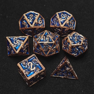 Puede incluir: Un conjunto de siete dados poliédricos de varias formas, incluyendo un d4, d6, d8, d10, d12 y d20. Los dados presentan un acabado de esmalte azul con detalles y numeración en metal dorado. Estos dados están diseñados para juegos de rol de mesa.
