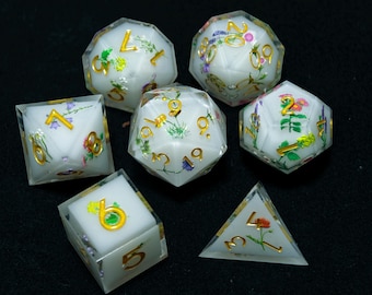 May include: A set of seven white dice with gold numbers and floral accents. The dice are in various shapes, including a d4, d6, d8, d10, d12, and d20.