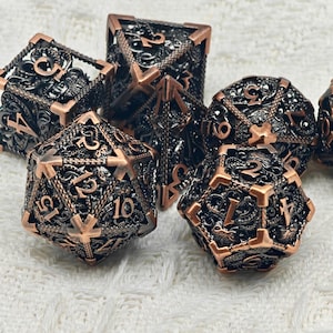 Peut inclure: Un ensemble de six dés en métal cuivre et noir avec des motifs complexes. Chaque dé a un nombre différent sur chaque face, de 1 à 6. Les dés sont parfaits pour les jeux de société.