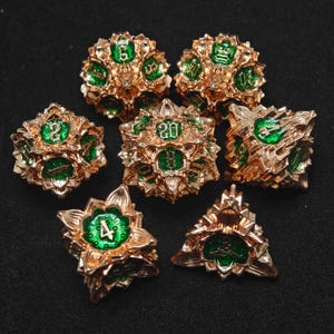 Op de afbeelding: Set van zeven gouden en groene metalen dobbelstenen met een bloemmotief. De dobbelstenen zijn genummerd 4, 6, 8, 10, 12, 20 en een d%.