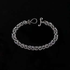 Könnte beinhalten: Ein silbernes Kettenarmband mit einem einzigartigen, ineinandergreifenden Design. Das Armband hat einen Verschluss.