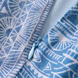 May include: Close-up of a blue and white patterned fabric with a zipper. The fabric features a geometric design with a light blue zipper pull. The overall aesthetic is clean and modern, suitable for apparel or home decor.