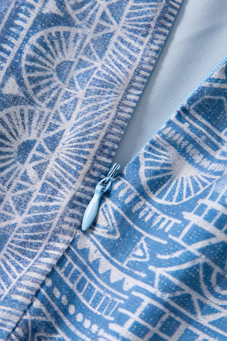 May include: Close-up of a blue and white patterned fabric with a zipper. The fabric features a geometric design with a light blue zipper pull. The overall aesthetic is clean and modern, suitable for apparel or home decor.