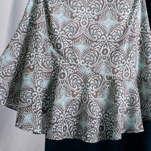 Op de afbeelding: Een uitlopende rok met een bruin en lichtblauw patroon. De stof heeft een herhalend bloemen- en geometrisch motief. De rok heeft een getailleerde taille en een uitlopende zoom, waardoor een vloeiend silhouet ontstaat.