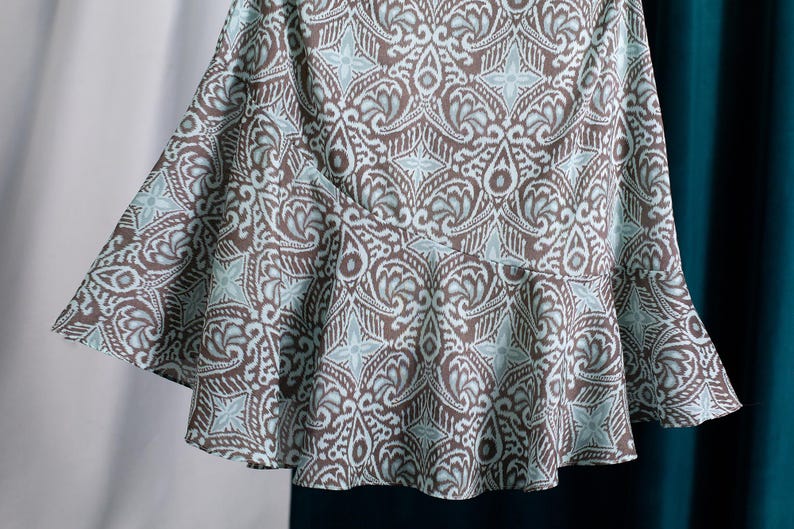 Op de afbeelding: Een uitlopende rok met een bruin en lichtblauw patroon. De stof heeft een herhalend bloemen- en geometrisch motief. De rok heeft een getailleerde taille en een uitlopende zoom, waardoor een vloeiend silhouet ontstaat.