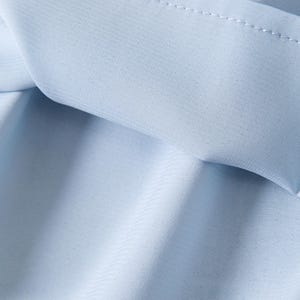 May include: Close-up of light blue fabric with visible stitching along the edges. The fabric appears to be soft and slightly textured, with subtle folds and shadows. The overall impression is of a delicate, flowing material.