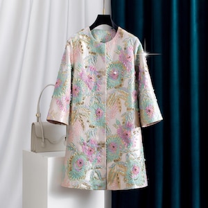 May include: A long-sleeved coat in a pale cream base colour featuring an intricate floral pattern in shades of pastel pink, mint green, and gold. The fabric has a textured, shimmering finish with scattered sequins throughout the floral design.