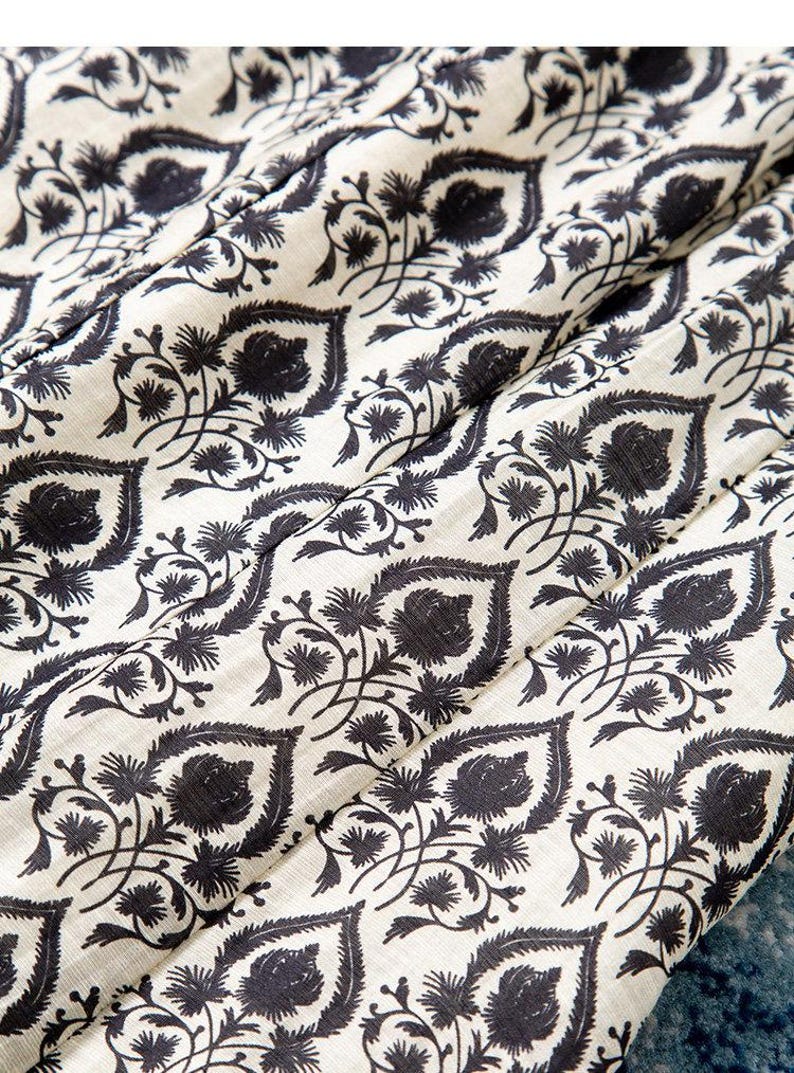 Op de afbeelding: Close-up van een stof met een herhalend patroon van donker marineblauwe bloemen- en bladmotieven op een gebroken witte achtergrond. De stof is gevouwen en toont de textuur en de drapering van het materiaal. Het ontwerp doet denken aan traditionele blokprints.