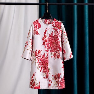 May include: A white coat adorned with a striking red floral design. The coat has a round neckline, three-quarter sleeves, and a knee-length cut. The floral pattern is detailed with gold accents, creating an elegant and eye-catching garment.
