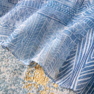 May include: Close-up of a blue and white patterned fabric with geometric designs. The fabric is draped over a textured surface with a mix of blue, white, and yellow tones. The pattern includes lines, shapes, and dotted details.