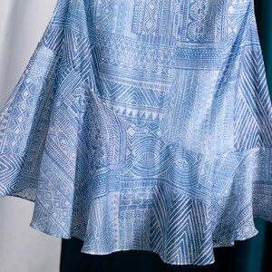 May include: A flowing, light blue skirt with a white geometric pattern. The fabric drapes gracefully, showcasing a detailed design of lines, triangles, and other shapes. The skirt has a ruffled hemline.