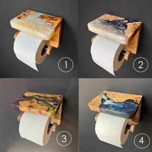 May include: Four wall-mounted toilet paper holders featuring a wooden shelf with integrated resin in various colors, including white, black, purple, green, and blue. Each holder includes a wooden dowel and a roll of white toilet paper.