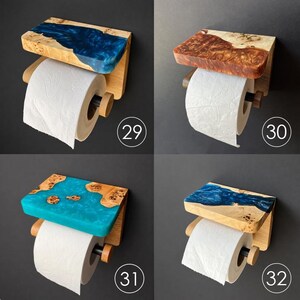 May include: Four wall-mounted toilet paper holders featuring a wooden shelf with embedded colored resin. Each unit includes a horizontal rod for a roll of white toilet paper. The designs are numbered 29, 30, 31, and 32, showcasing blue, brown, and turquoise resin.