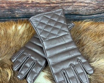 May include: A pair of brown quilted leather gloves. The gloves have a diamond pattern on the back of the hand and a ribbed design on the fingers. The gloves are displayed on a brown and tan fur surface.
