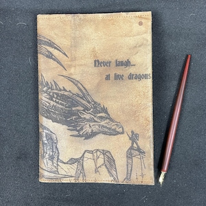 May include: A brown leather journal with a dragon illustration and the text "Never laugh... at live dragons".