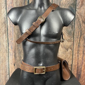 May include: A brown leather belt with a brass buckle and a matching brown leather shoulder strap. The strap has a brass buckle and is attached to a brown leather pouch.