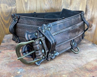 May include: A brown leather belt with a decorative buckle and multiple straps. The belt has a distressed look and features metal accents.