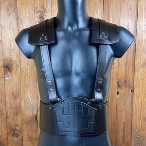 May include: A black leather chest protector with straps and a decorative cross design. The chest protector is worn on a mannequin.