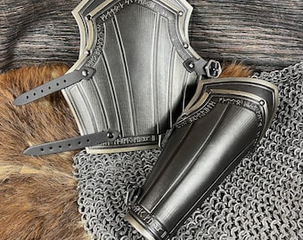 May include: A pair of black metal arm guards with silver accents and leather straps. The guards are decorated with intricate patterns and runes.