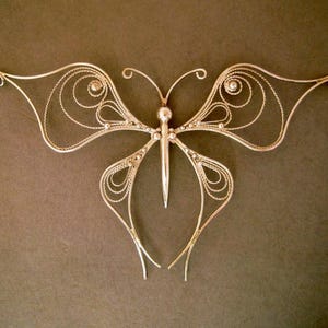 May include: A silver butterfly necklace with intricate wirework details. The butterfly has a delicate, airy design and is suspended from a thin chain.