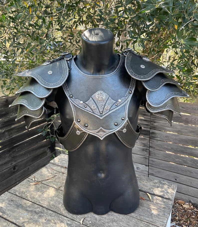 May include: Black and silver fantasy armor set displayed on a mannequin. The armor features layered shoulder pauldrons, a chest plate with decorative silver trim, and rivet details. The armor is designed to protect the torso and shoulders.