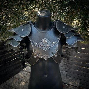 May include: Black and silver fantasy armor set, displayed on a mannequin. The chest piece and shoulder pauldrons are detailed with ornate silver accents and rivets. The armor is designed with layered plates and decorative edges, suggesting a medieval or fantasy theme.