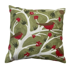 May include: Green square throw pillow with embroidered design. The pillow features a white tree with red berries and brown and red birds. The pillow is a decorative item for a couch or bed.