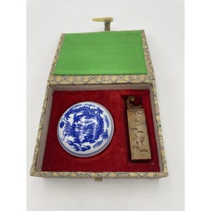 May include: An antique Chinese seal set in a decorative box. The set includes a round, white porcelain ink well with a blue dragon design, and a rectangular seal with carved imagery. The box has a red velvet interior and green silk lining.