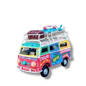 Peut inclure: Un van jouet coloré peint à la main avec une planche de surf, une bouée de sauvetage et des bagages sur le toit. Le van est décoré de couleurs vives et de motifs, y compris des citrons et des volutes.