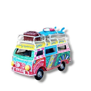 Peut inclure: Un van jouet en métal peint à la main, coloré, avec une planche de surf et des bagages sur le porte-bagages. Le van est décoré de volutes et de motifs dans des tons de rouge, jaune, bleu, vert et blanc.