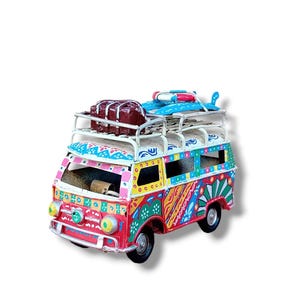 Peut inclure: Un van jouet coloré peint à la main avec un toit blanc et un porte-bagages sur le dessus. Le van est décoré de couleurs vives et de motifs, notamment du rouge, du jaune, du bleu, du vert et du rose. Le van a une planche de surf et une valise brune sur le porte-bagages.