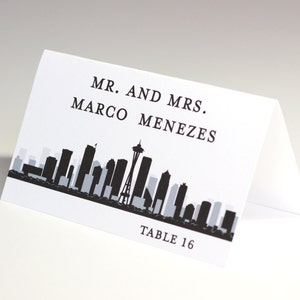 Tarjeta de lugar impresa con el horizonte de Seattle con el nombre del invitado y la mesa, elija el color y la fuente que combinen con su boda o evento, llega doblada