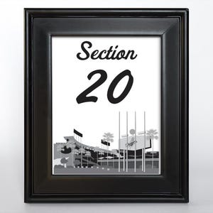 May include: Black framed print with the text "Section 20" in a bold font. The print shows a grayscale stadium illustration with palm trees and the Dodgers logo. The frame is solid black, suitable for wall display.