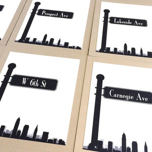 Puede incluir: Cuatro tarjetas imprimibles en blanco y negro con una silueta del horizonte de Cleveland y una señal de calle. Las señales de calle dicen "Prospect Ave", "Lakeside Ave", "W 6th St" y "Carnegie Ave".