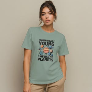 May include: A light green t-shirt with the text "WHEN I WAS YOUNG WE HAD 9 PLANETS" and a graphic of planets. The planets are in shades of orange, blue, and brown. The shirt has short sleeves.