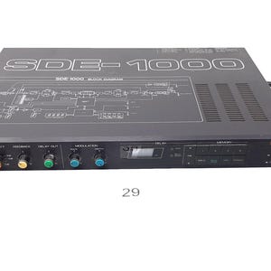 May include: A black Roland SDE-1000 digital delay unit with a silver display and a variety of knobs and buttons. The unit has a black power cord and a black cable.