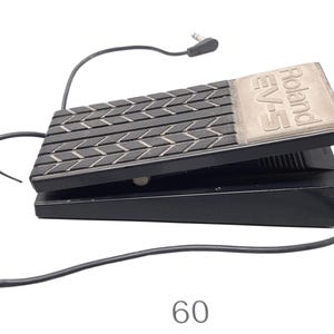 May include: Black Roland EV-5 expression pedal with a textured black footpad and a silver plate with the Roland EV-5 logo. The pedal is connected to a black cable with a 1/4 inch jack.