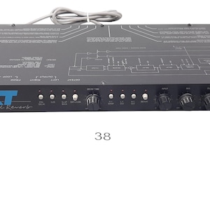 Può includere: Unità di riverbero digitale nera con la scritta "XT Digital Reverb" in blu. Presenta manopole, pulsanti e un interruttore di alimentazione. Un diagramma è stampato sulla superficie superiore. Un cavo grigio si estende dalla parte superiore.